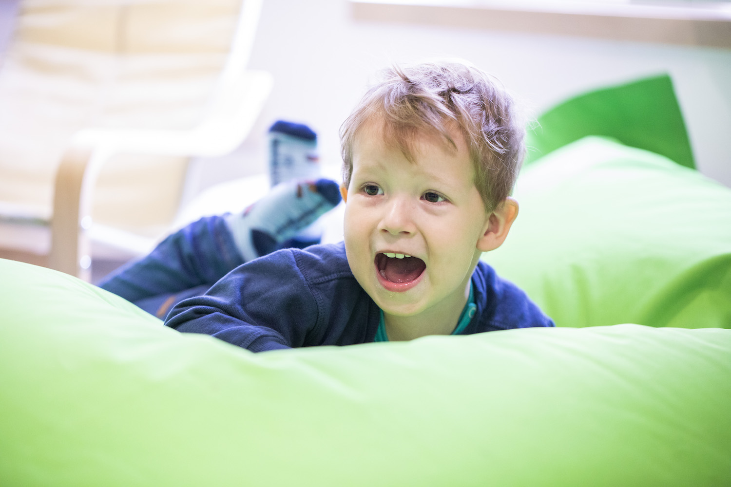 Kleiner Junge liegt bäuchlings auf einem großen Sitzsack und lacht