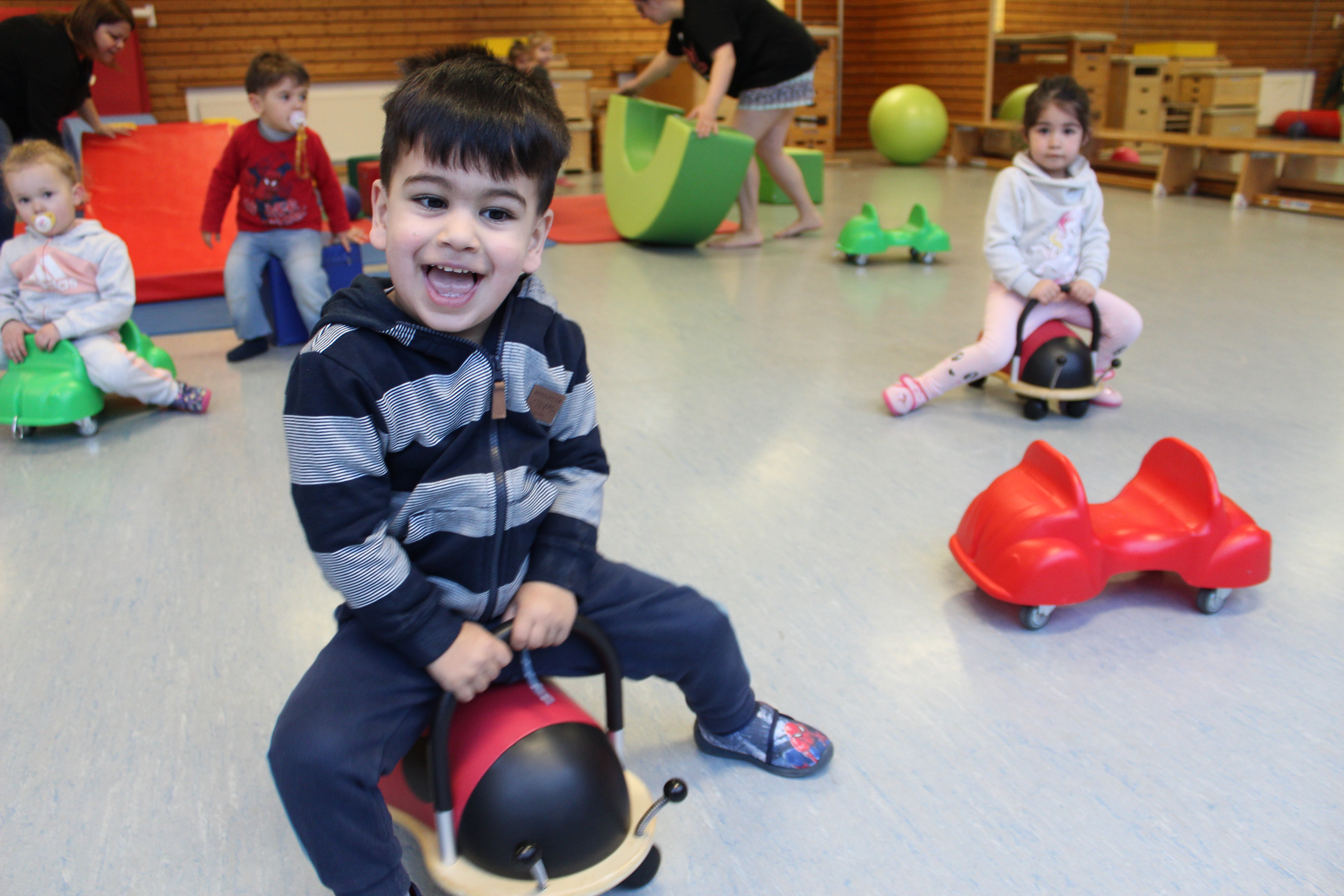 Vier Kinder fahren auf Bobbycars durch eine Turnhalle