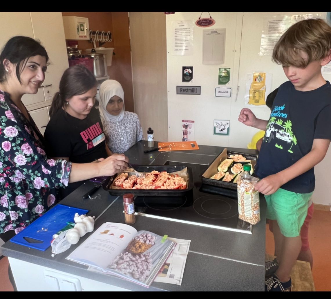 Eine Frau und drei Kinder stehen um eine Kochinsel und legen gefüllte Paprika und Zucchini auf ein Backbleche.
