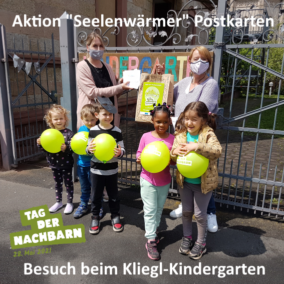 Fünf Kinder mit gelben Ballons stehen vor einem Zaun, dahinter stehen zwei Frauen, die eine Tüte hochhalten