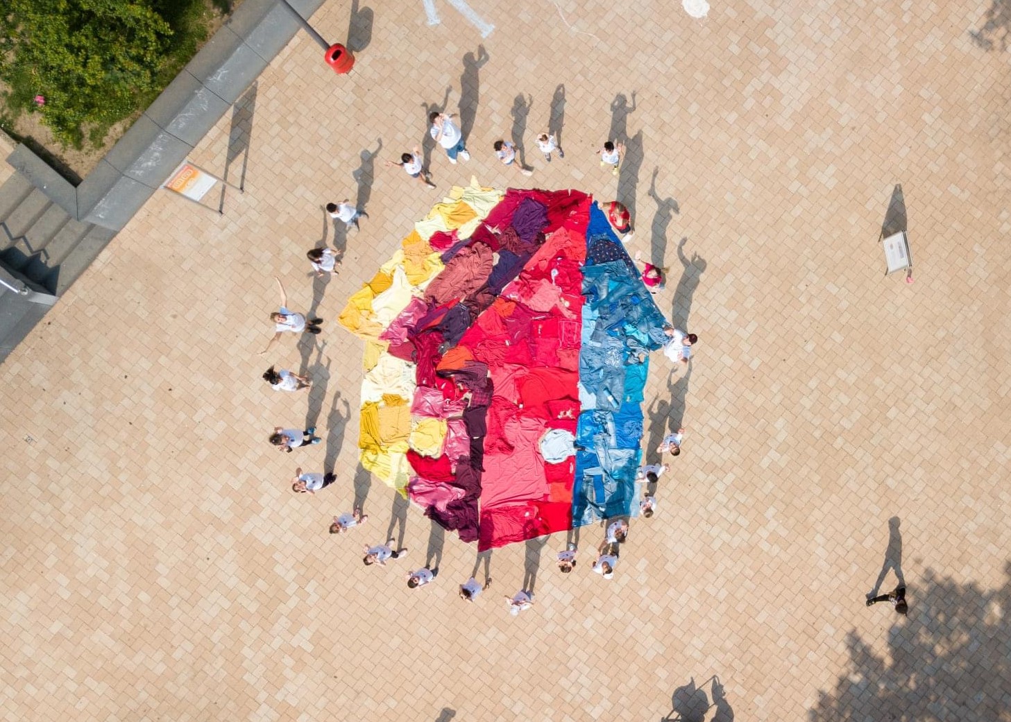 Aufnahme von oben: Viele Menschen in weißen T-Shirts stehen um ein aus gefärbtem Stoff auf den Boden gelegtes Mehrgenerationenhaus-Logo