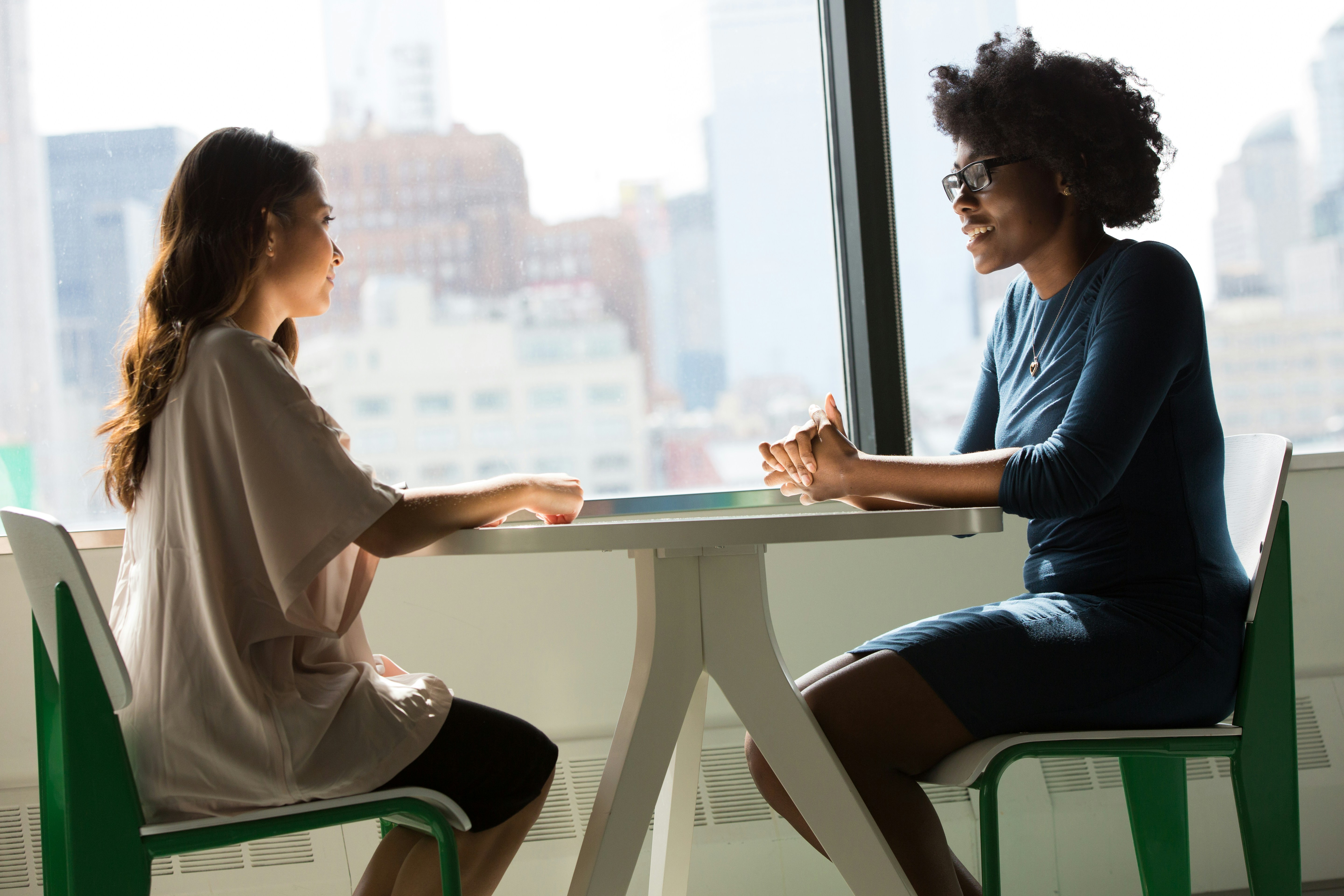 Zwei Frauen sitzen sich an einem runden Tisch gegenüber und sprechen miteinander.