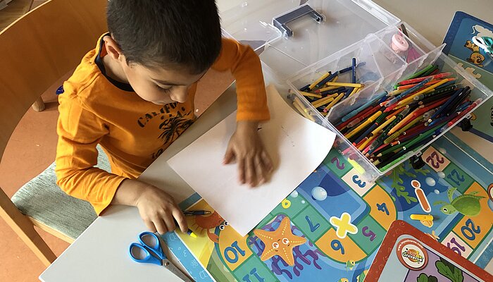 Ein junge mit gelbem Shirt sitzt an einem Kindertisch und malt