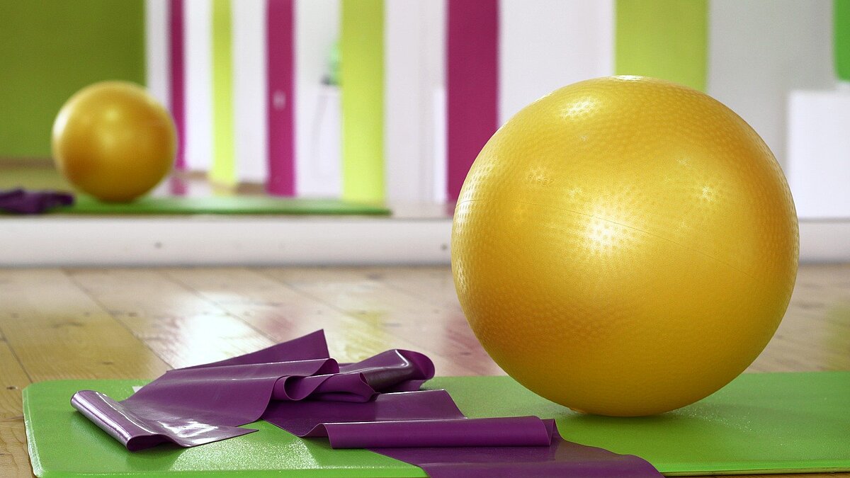Gymnastikmatte, Gymnastikband und Gymnastikball auf dem Boden einer Turnhalle liegend