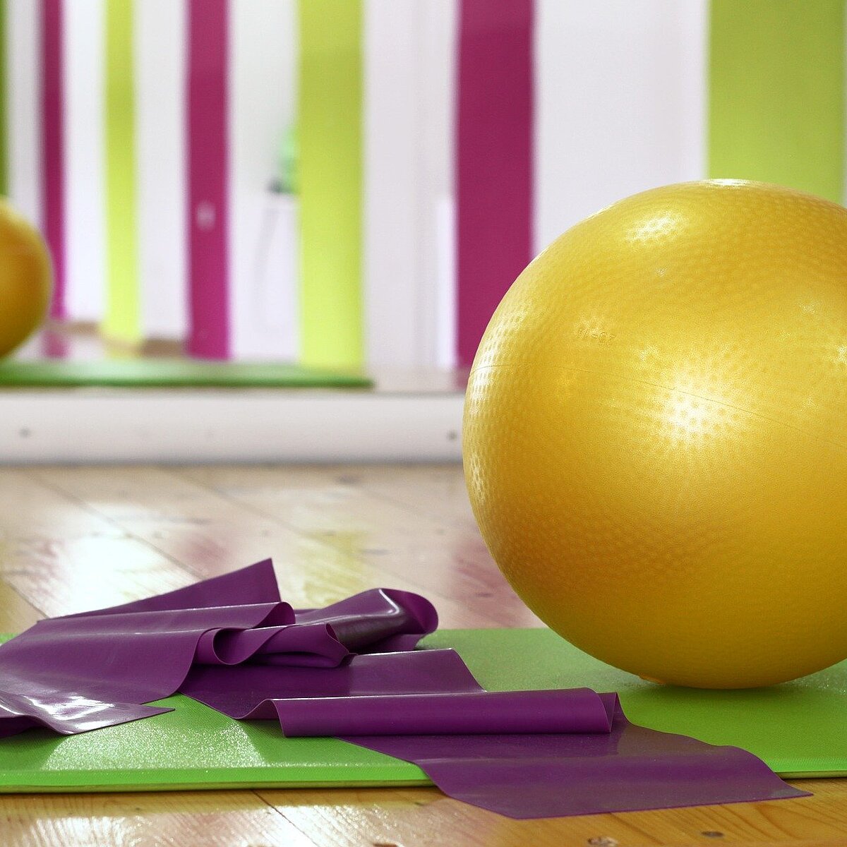 Gymnastikmatte, Gymnastikband und Gymnastikball auf dem Boden einer Turnhalle liegend