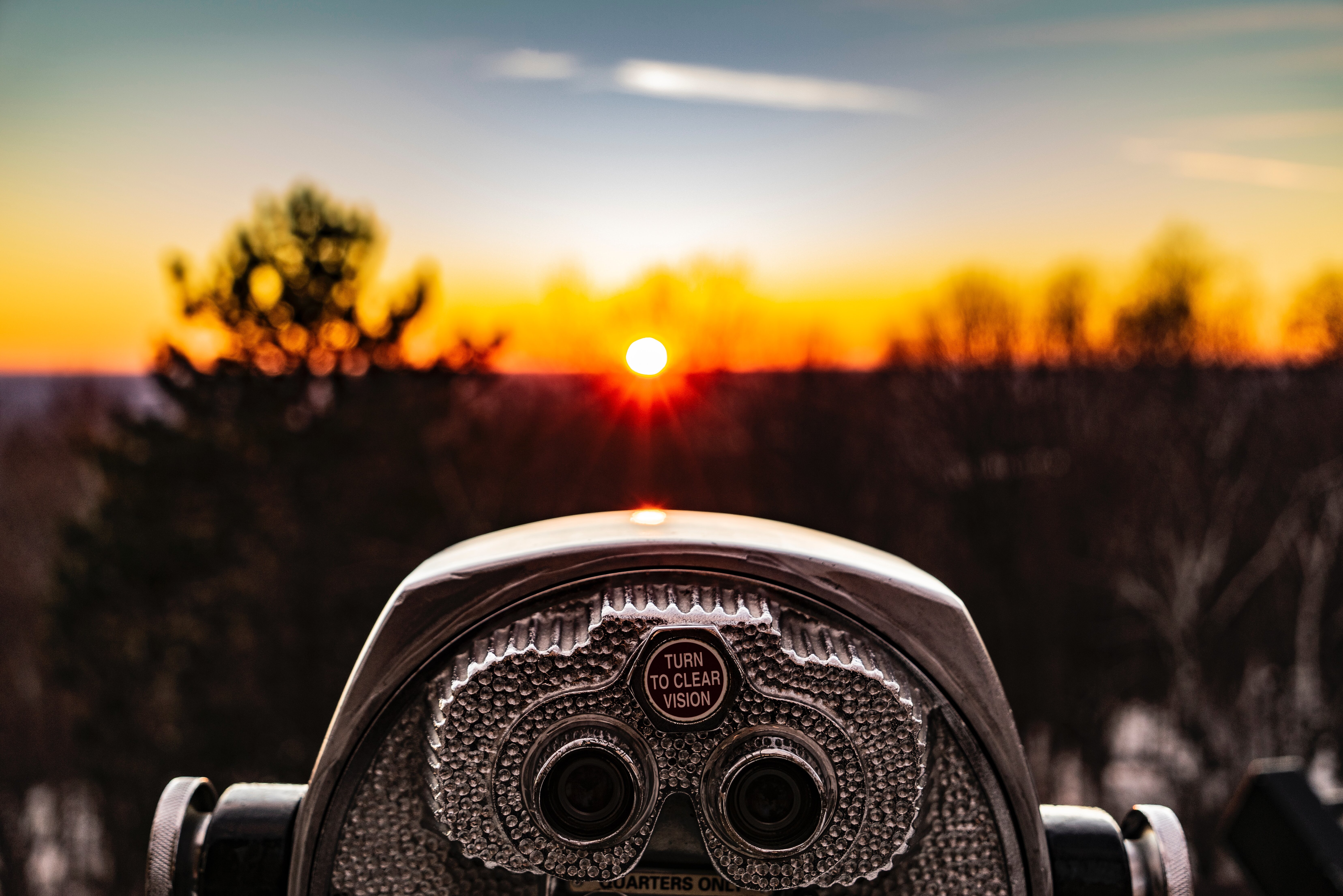 Fernglas im Vordergrund, welches in Richtung der untergehenden Sonne zeigt.