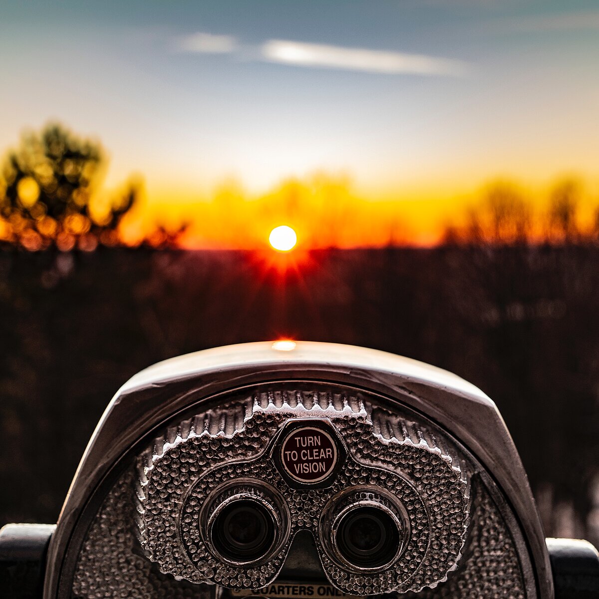 Fernglas im Vordergrund, welches in Richtung der untergehenden Sonne zeigt.