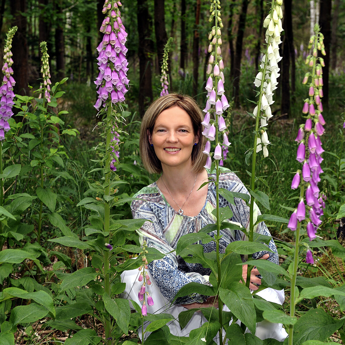 Frau hockt in einem Beet umringt von Blumen