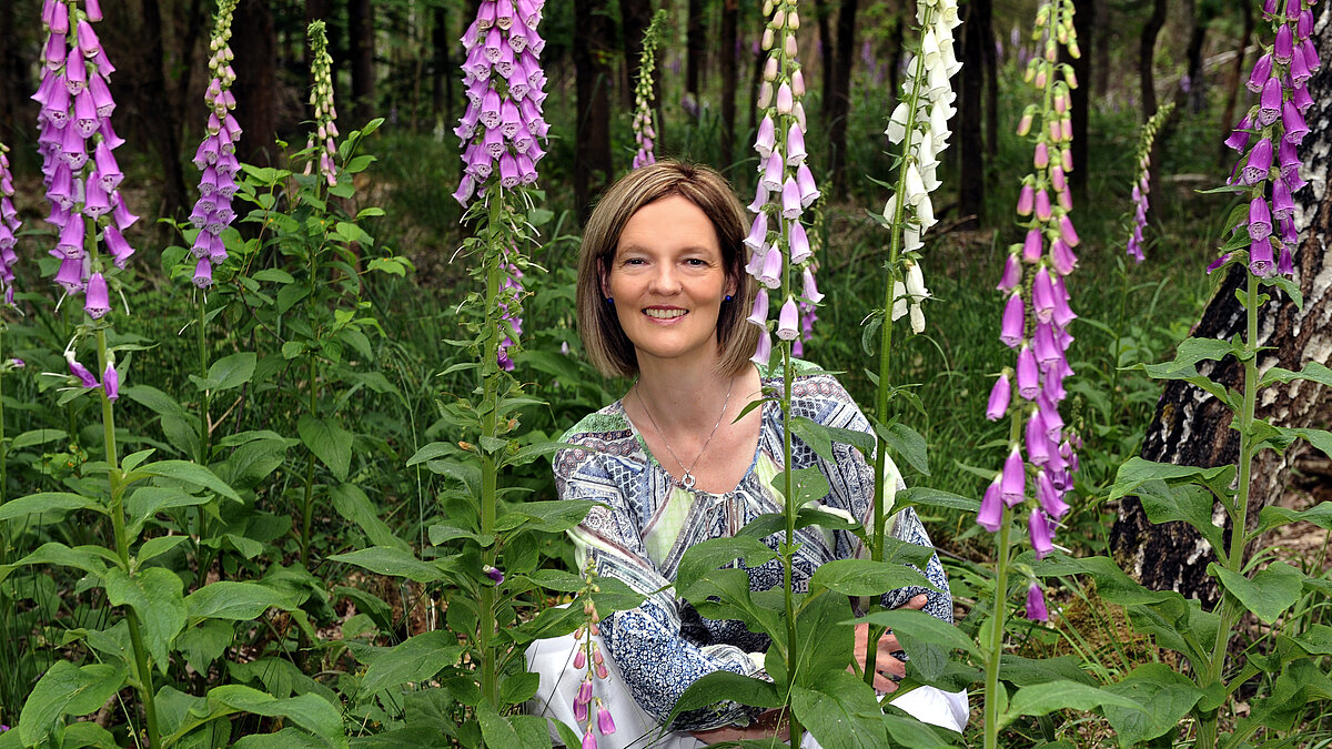 Frau hockt in einem Beet umringt von Blumen