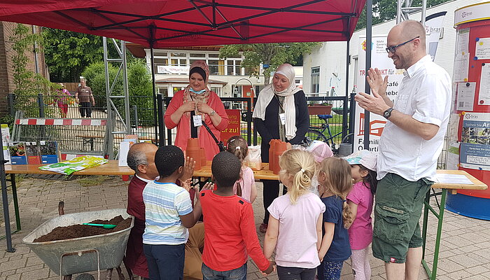 Zwei Frauen stehen hinter einem Biertisch unter einem Unterstand, ein Mann steht mit sechs Kindern davor