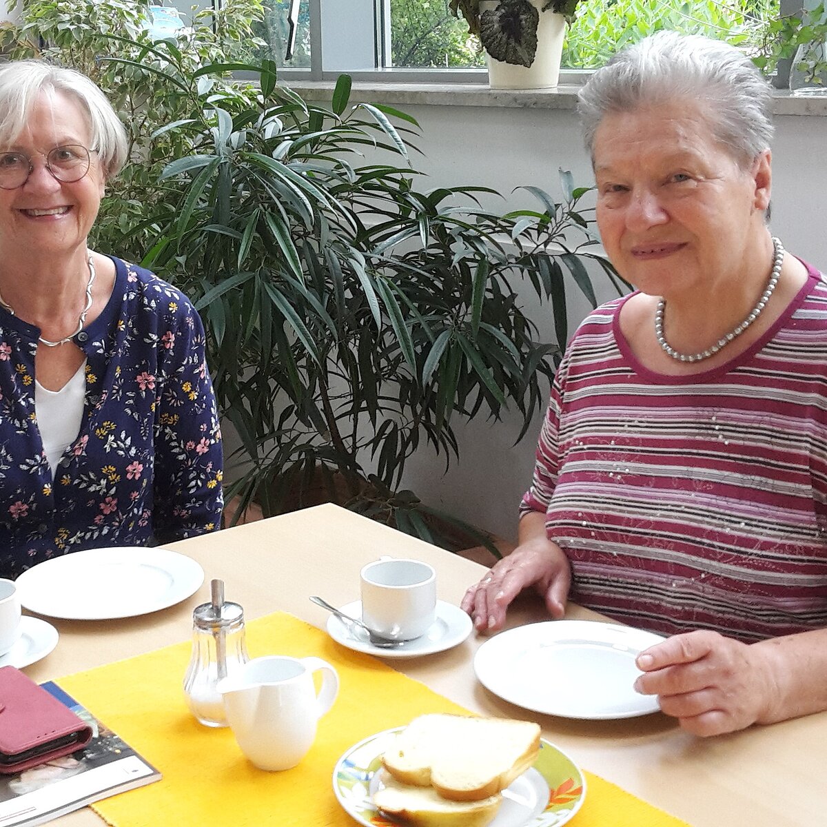 Zwei ältere Damen sitzen zusammen am Tisch und trinken Kaffee. 