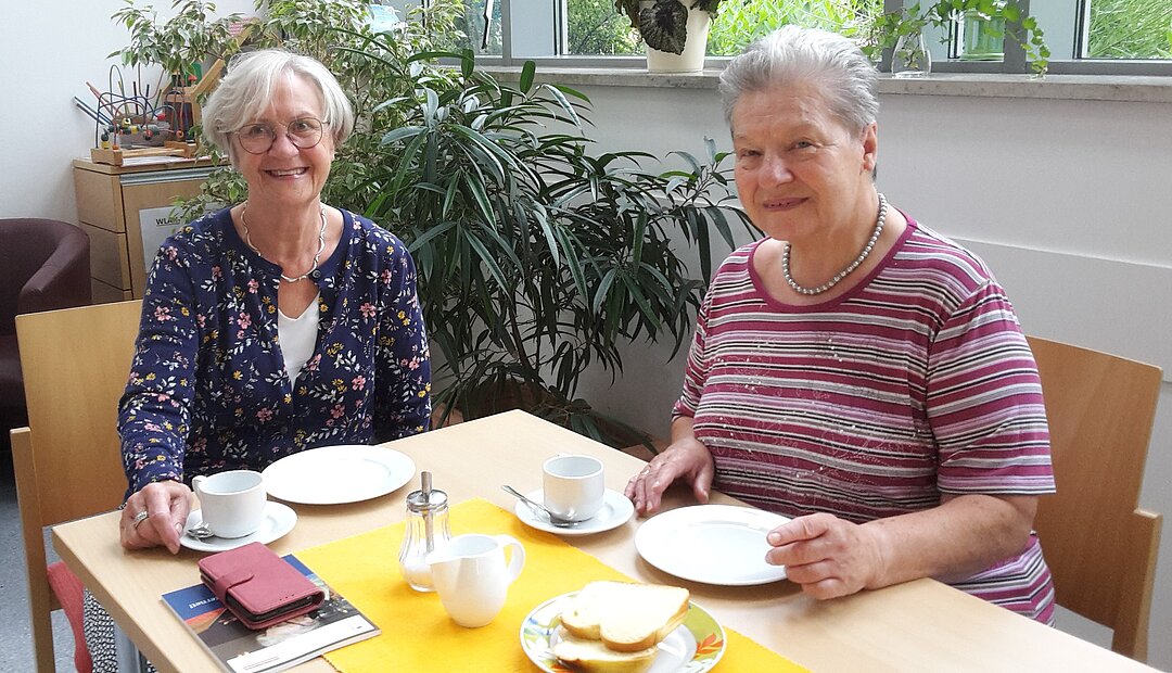 Zwei ältere Damen sitzen zusammen am Tisch und trinken Kaffee. 