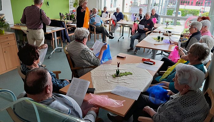 Seniorinnen und Senioren sitzen an Tischen und haben Tüll-Tücher in den Händen