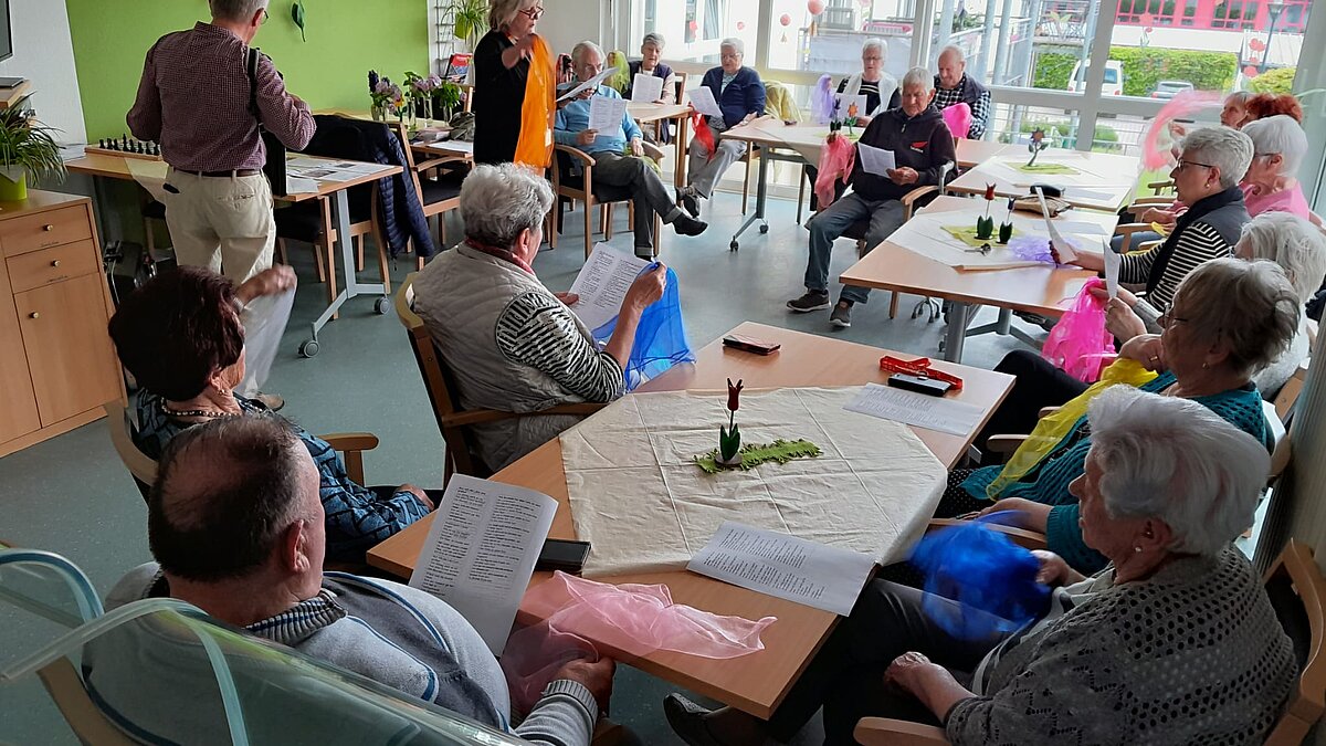 Seniorinnen und Senioren sitzen an Tischen und haben Tüll-Tücher in den Händen