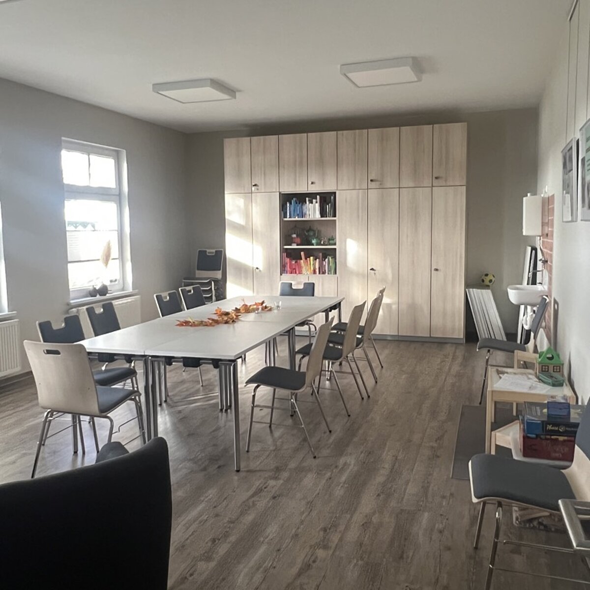 Der Clubraum fotografiert aus der hinteren rechten Ecke. Zu sehen sind eine kleine Lounge-Ecke, der Kinder-Spieltisch und die große Tafel mit Stühlen in der Mitte.