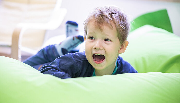Kleiner Junge liegt bäuchlings auf einem großen Sitzsack und lacht
