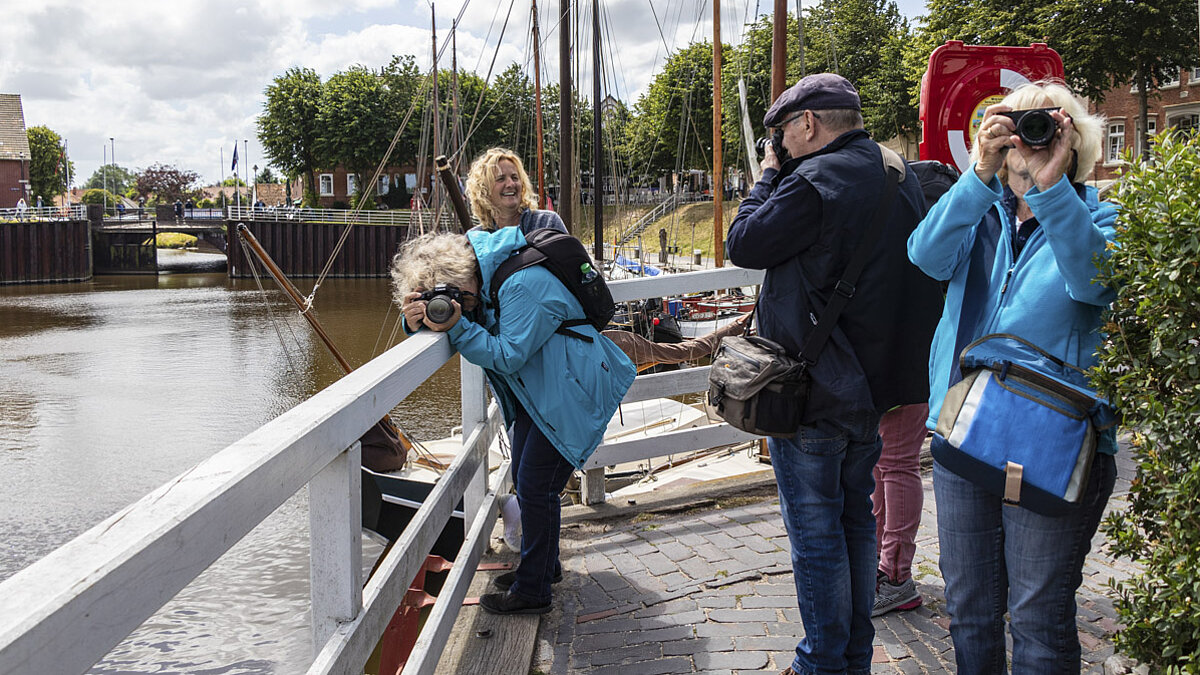 Vier Personen stehen am Wasser und suchen Motive mit Spiegelreflexkameras. 