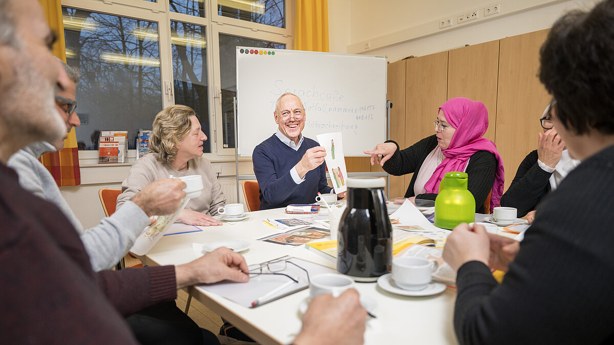Sechs Personen sitzen an einem Tisch mit Kaffeetassen sowie Blättern und Broschüren in der Mitte
