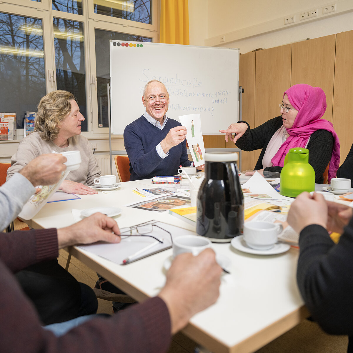 Sechs Personen sitzen an einem Tisch mit Kaffeetassen sowie Blättern und Broschüren in der Mitte