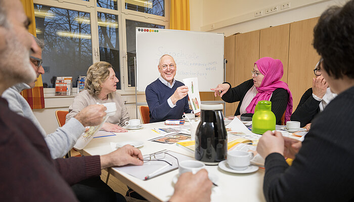 Sechs Personen sitzen an einem Tisch mit Kaffeetassen sowie Blättern und Broschüren in der Mitte