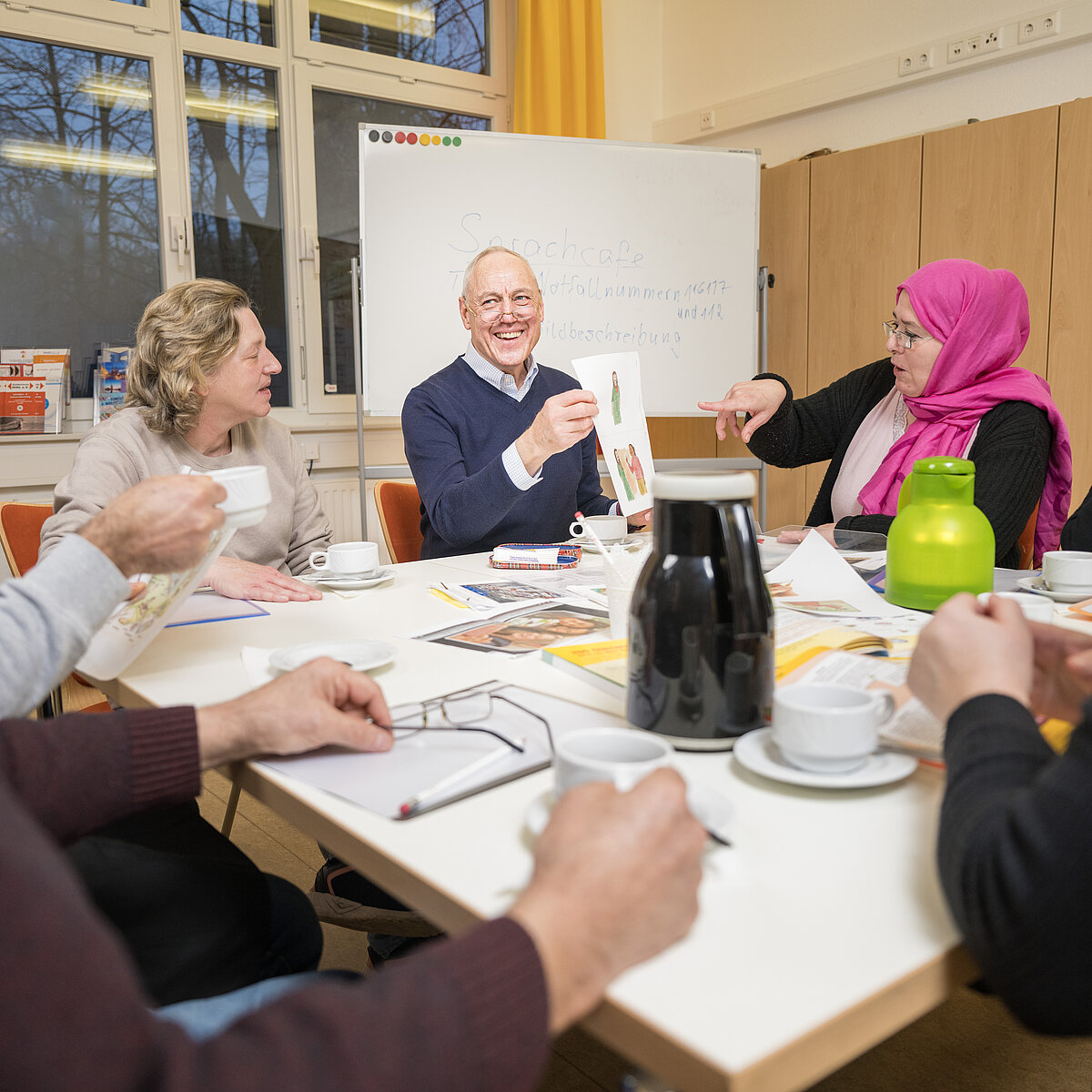 Sechs Personen sitzen an einem Tisch mit Kaffeetassen sowie Blättern und Broschüren in der Mitte