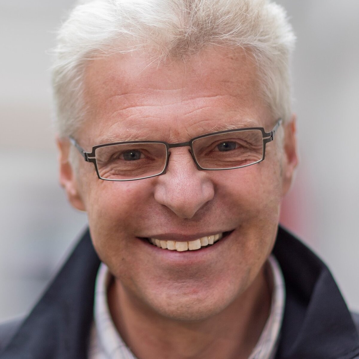 Porträt von Dr. Hermann Scheuerer-Englisch mit grauen Haaren, Brille und blauer Jacke