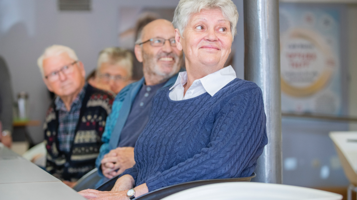 Seniorinnen und Senioren sitzen lächelnd an einem Tisch