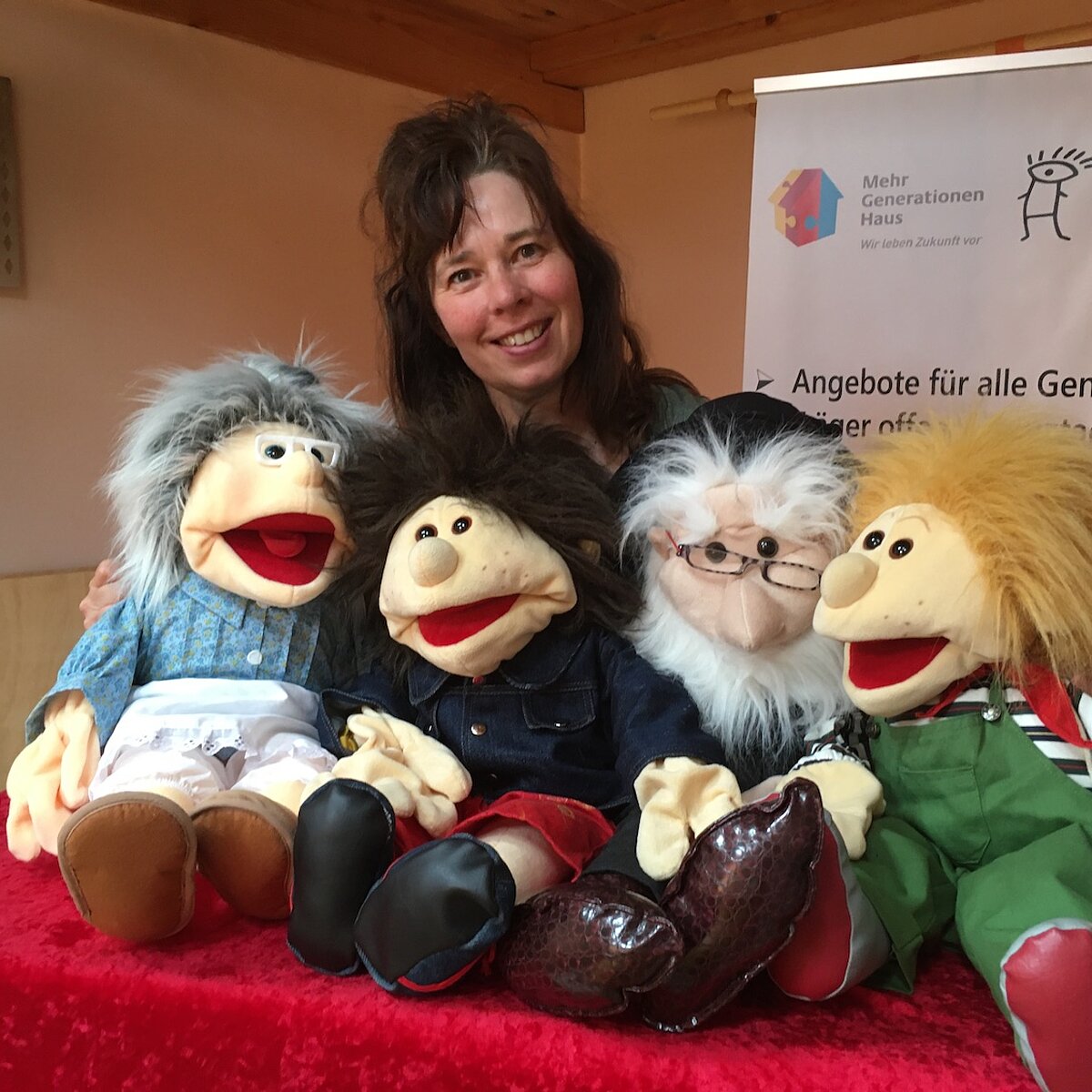 Frau steht hinter einem Tisch, auf dem vier Handpuppen sitzen