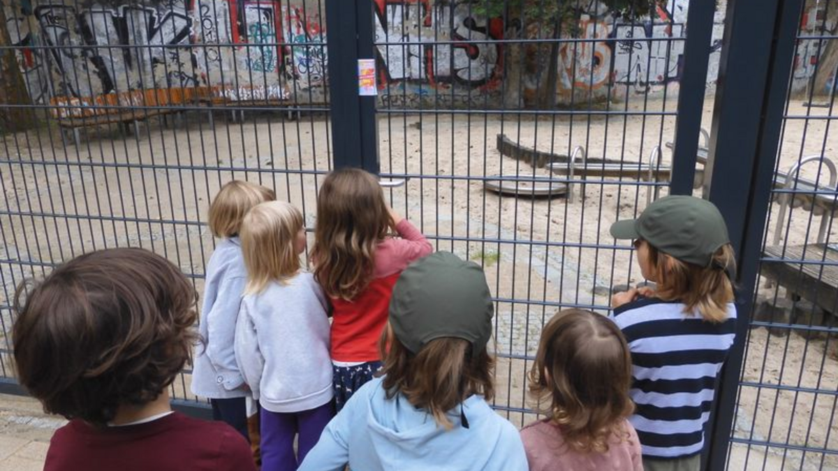 Sieben Kinder stehen vor dem Zaun eines Spielplatzes