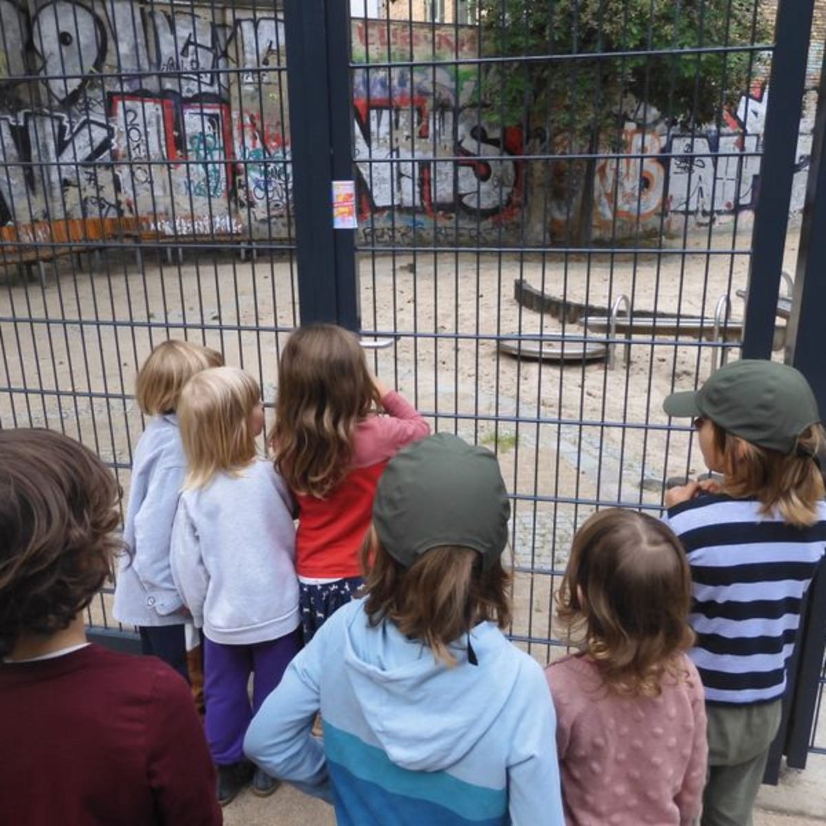 (c) Kiezanker 36 Sieben Kinder stehen vor dem Zaun eines Spielplatzes