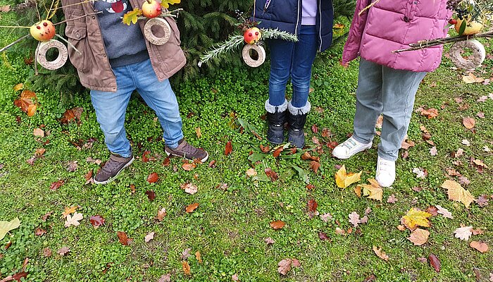 Kinder stehen auf einer Wiese und zeigen Basteleien.