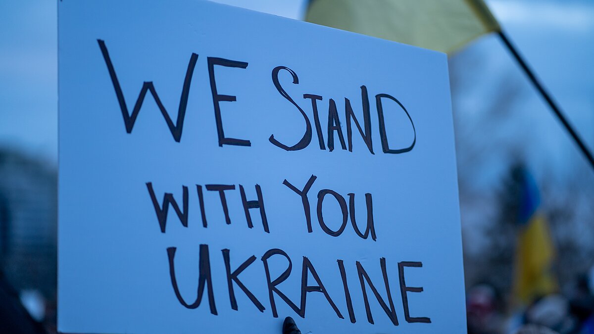 Pappschild mit der Aufschrift "We stand with you Ukraine"