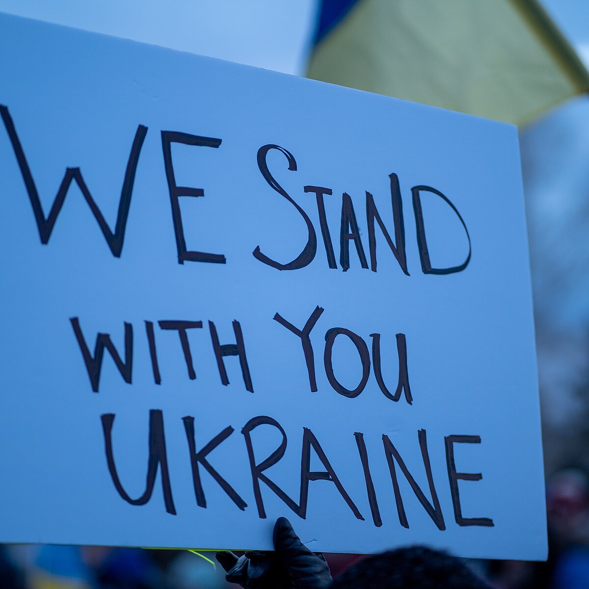 Pappschild mit der Aufschrift "We stand with you Ukraine"