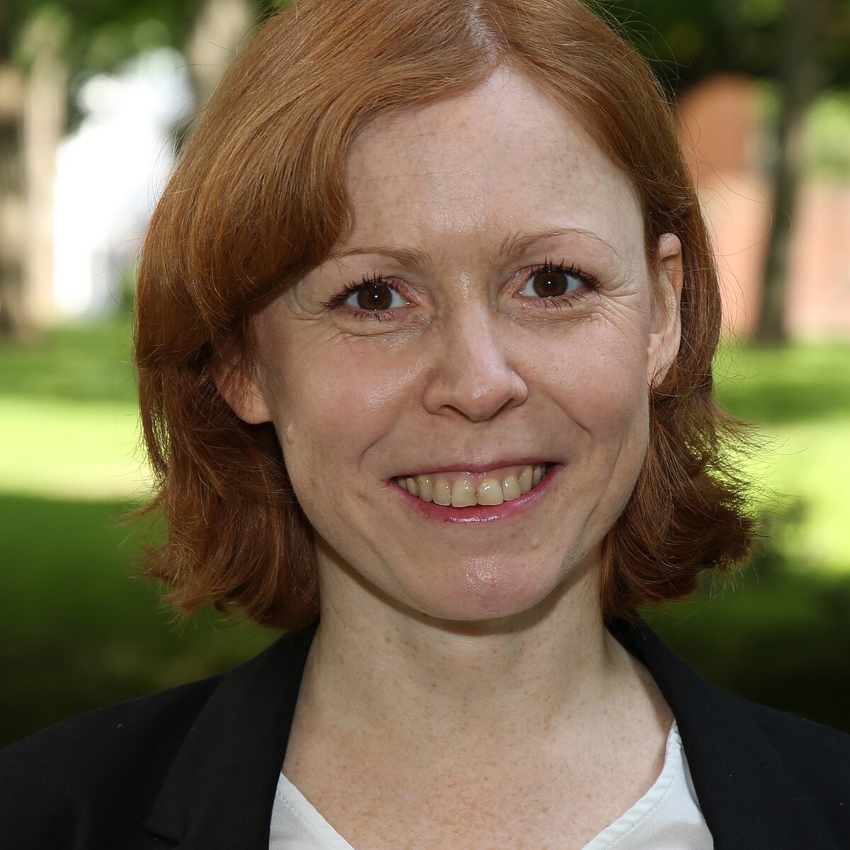 Eine mittelalte Frau mit roten Haaren lacht in die Kamera.