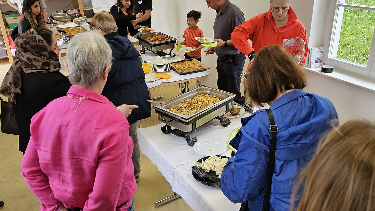 Menschen stehen an einem Buffet und nehmen sich Essen