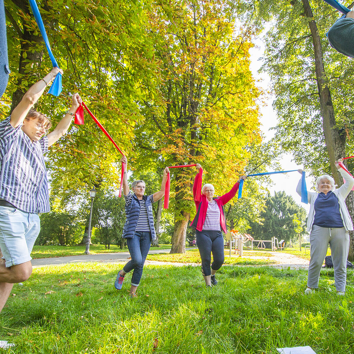 Mehrere Menschen bewegen sich mit Bändern in einem Park.