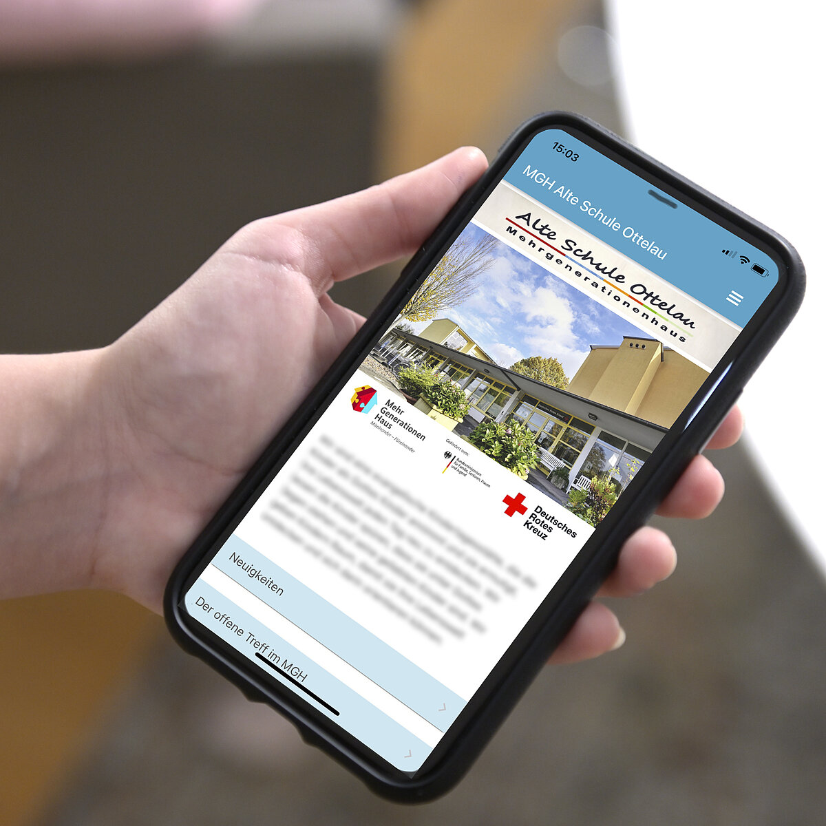 Hand hält ein Handy, auf dem die App des Mehrgenerationenhauses Alte Schule Ottelau zu sehen ist