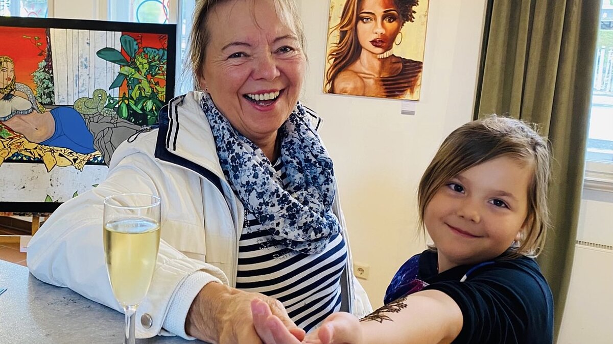 Eine Frau und ein Mädchen lachen in die Kamera. Das Mädchen zeigt ihr Hanna Tattoo. 