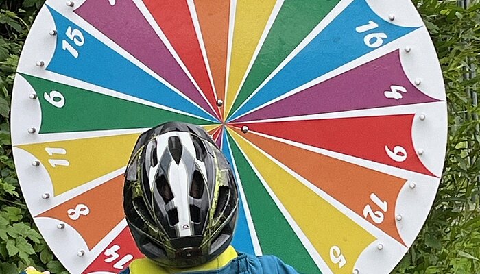 Kind mit Fahrradhelm steht vor einem Glücksrad