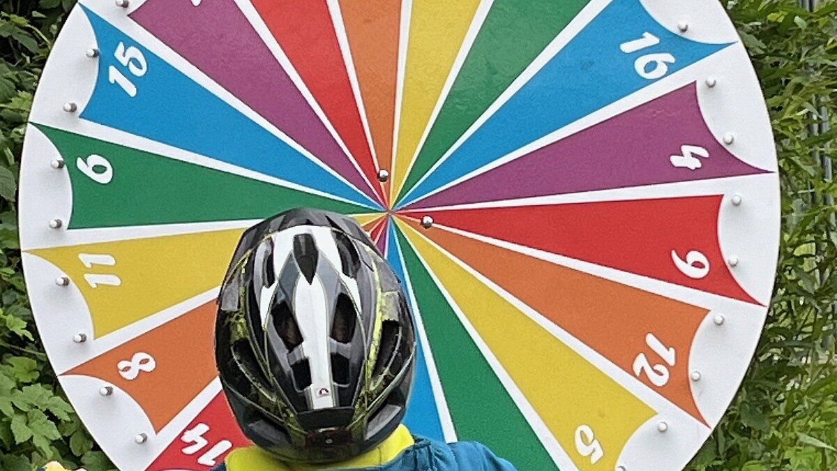 Kind mit Fahrradhelm steht vor einem Glücksrad