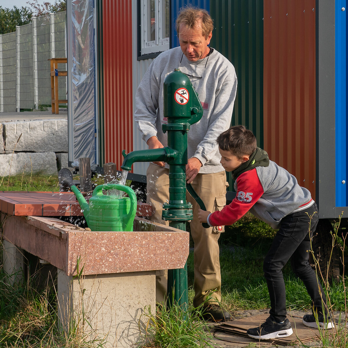 Ein Mann und ein Junge pumpen Wasser aus einem Brunnen in eine Gießkanne