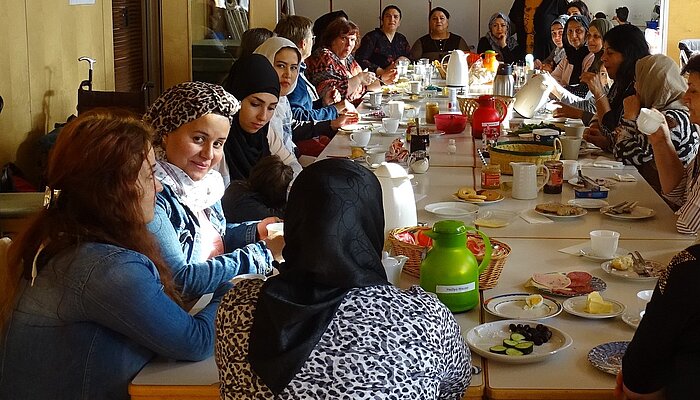 21 Frauen sitzen an einem großen Tisch und frühstücken
