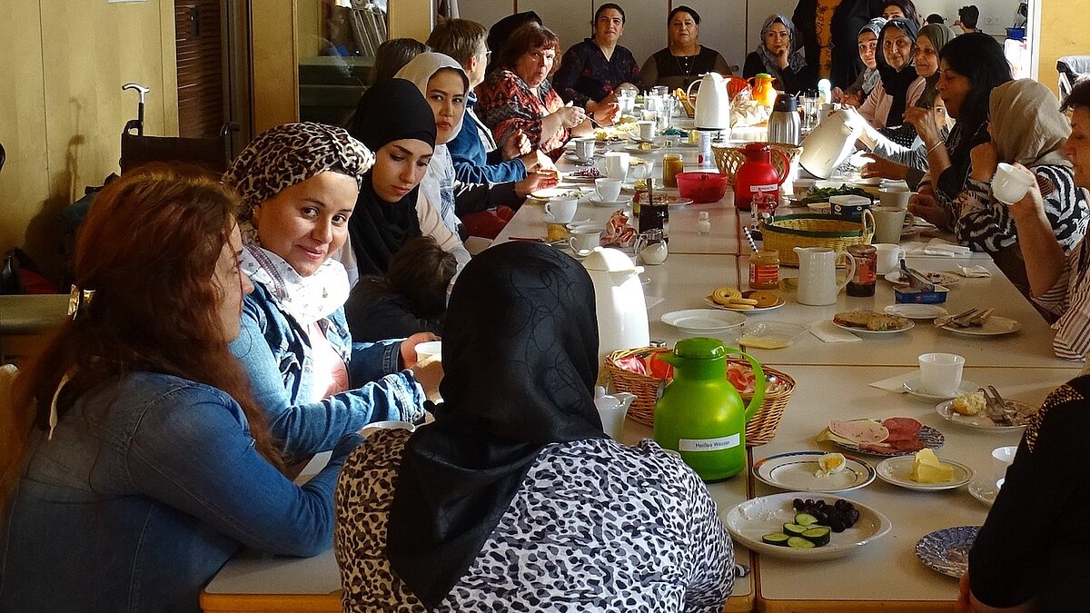 21 Frauen sitzen an einem großen Tisch und frühstücken