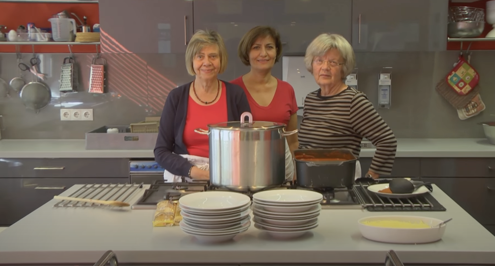Drei ältere Frauen stehen in einer Küche mit einer großen Kochinsel.