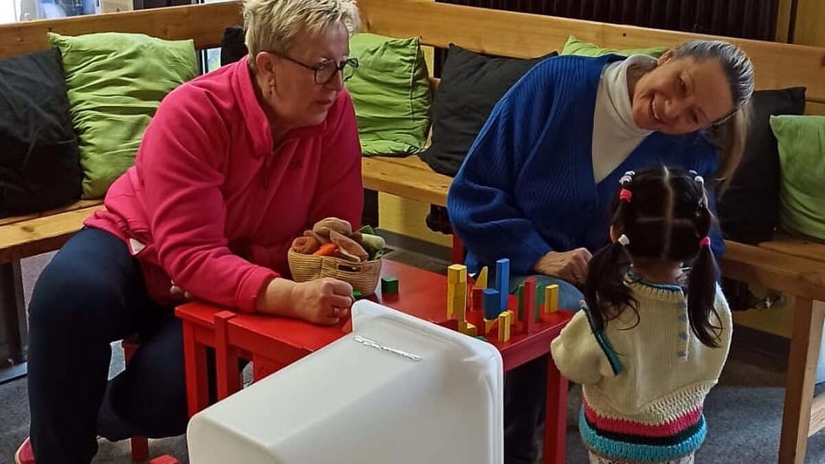 Zwei Frauen spielen mit einem Kleinkind an einem Tisch mit Bauklötzen
