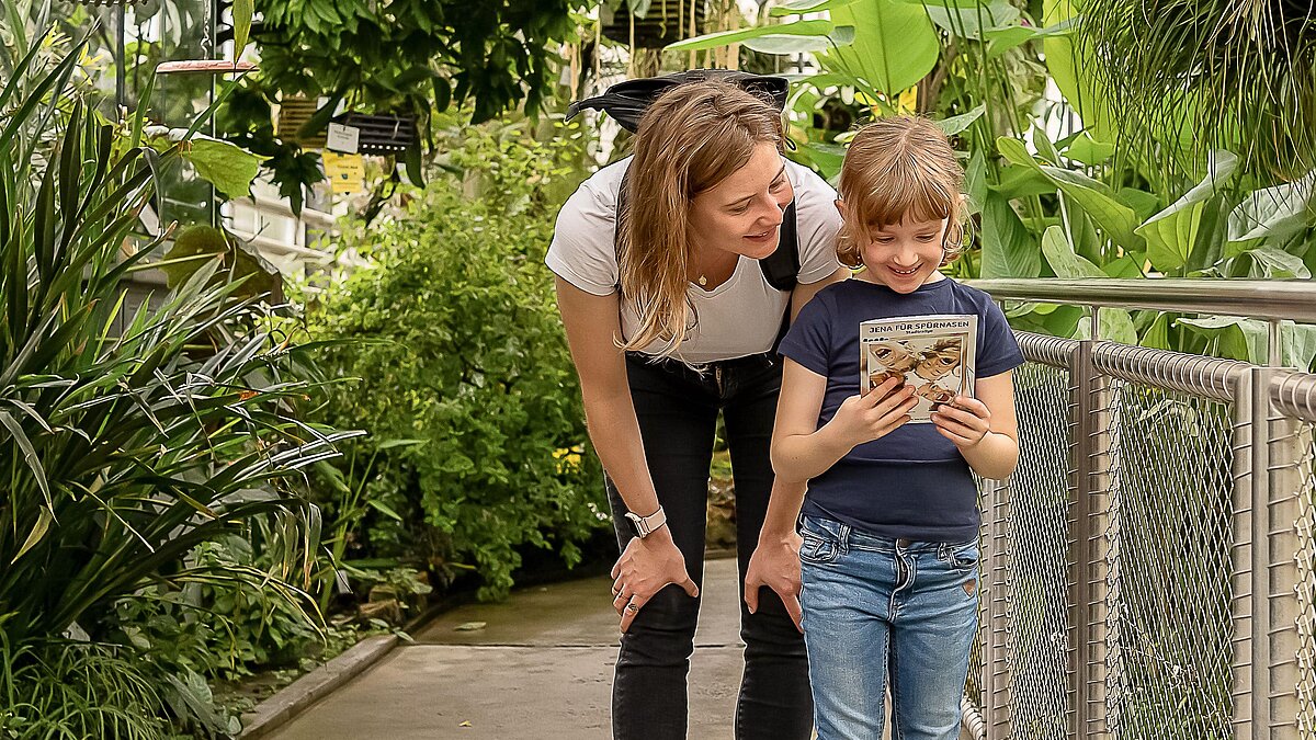 Ein Kind und eine Frau stehen zusammen in einem großen Tropenhaus eines Botanischen Gartens.