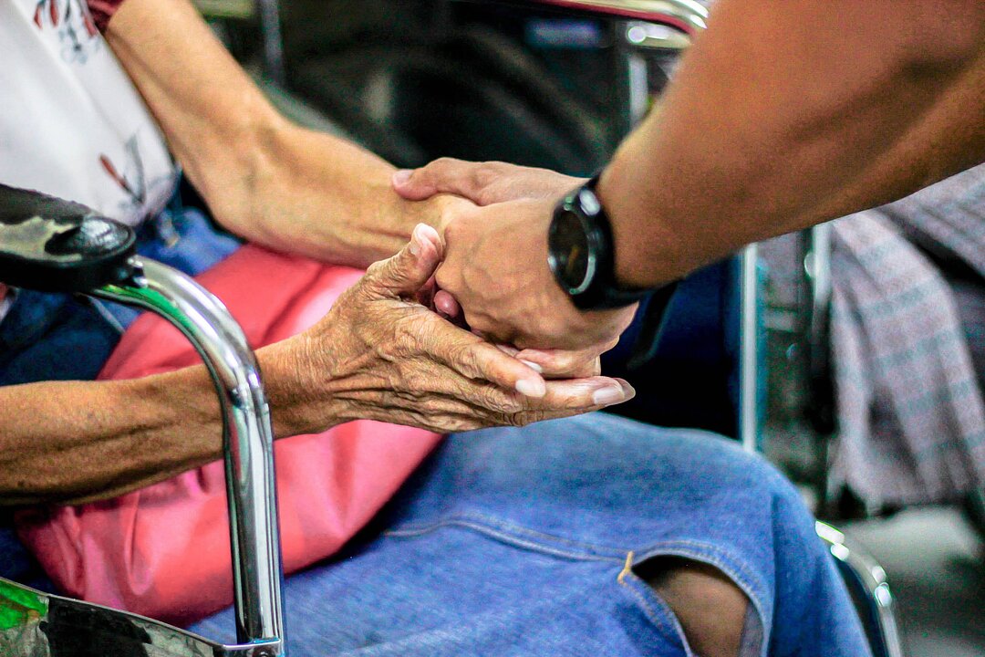 Hände einer Älteren Frau halten die Hand eines Mannes. 