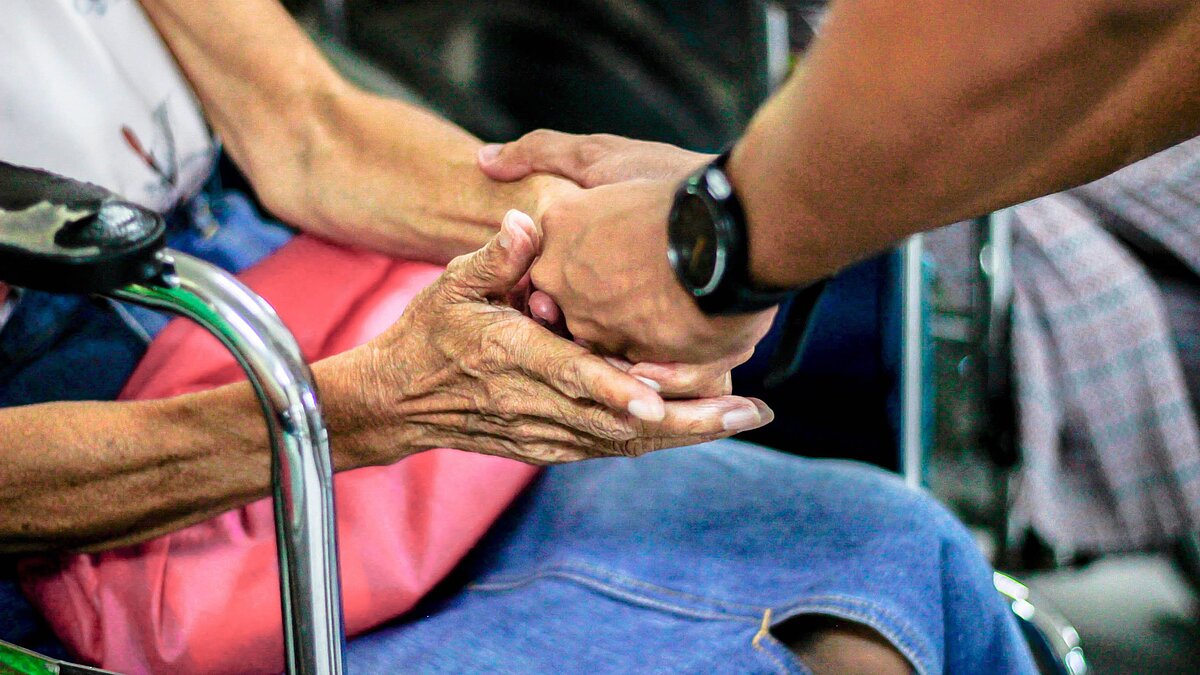 Hände einer Älteren Frau halten die Hand eines Mannes. 