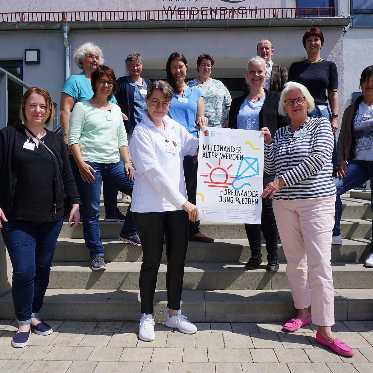 Teilnehmerinnen und Teilnehmer der Fachgruppe Qualitätskriterien stehen auf der Treppe vor dem Mehrgenerationenhaus Weidenbach