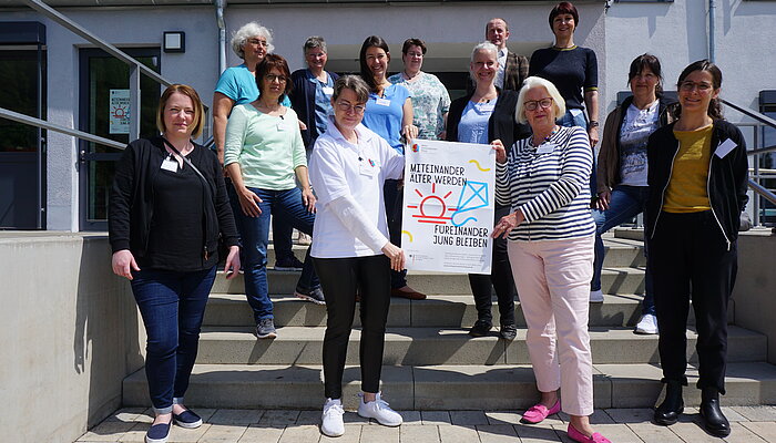 Teilnehmerinnen und Teilnehmer der Fachgruppe Qualitätskriterien stehen auf der Treppe vor dem Mehrgenerationenhaus Weidenbach